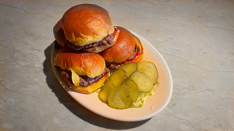 Four sliders on a plate with lettuce and pickles neatly arranged on the side
