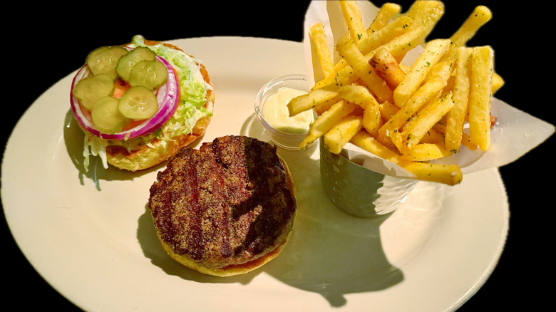 The Old Fashioned Burger split open to reveal pickles and meat, with a side of truffle fries and aioli