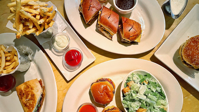 A few of Cheesecake Factory's signature Glamburgers and a side of truffle fries and salad on a table