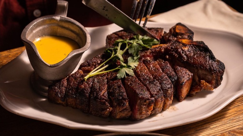 Sliced porterhouse steak on a white plate with béarnaise sauce in a pitcher