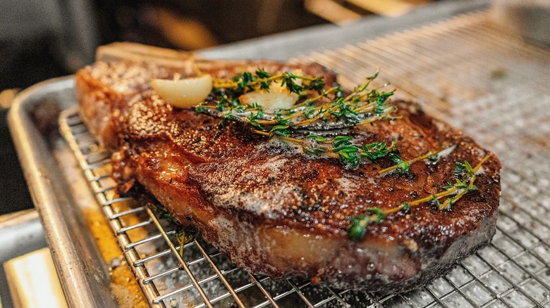 Butter-basted bone-in ribeye steak on a cooling rack garnished with fresh thyme