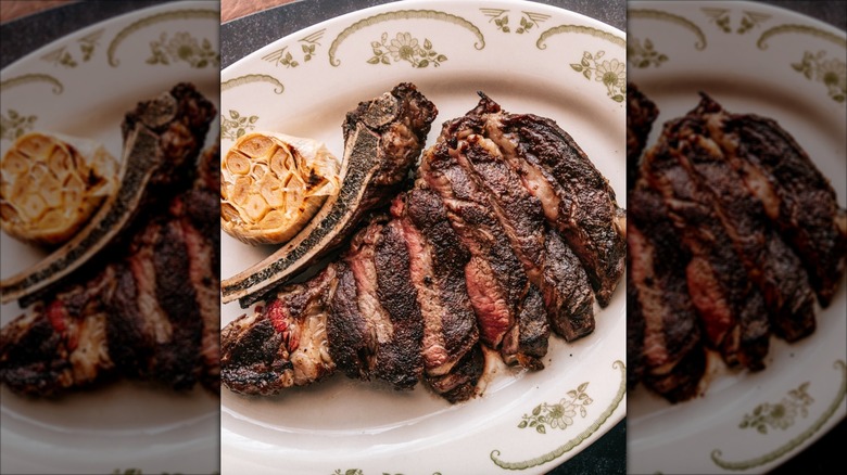 Sliced bone-in ribeye on a white plate with roasted garlic