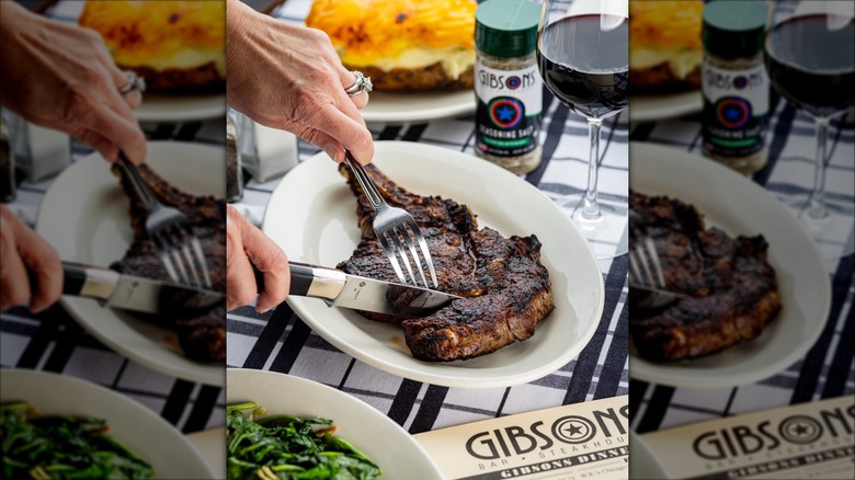 Person eating a bone-in ribeye on a white plate
