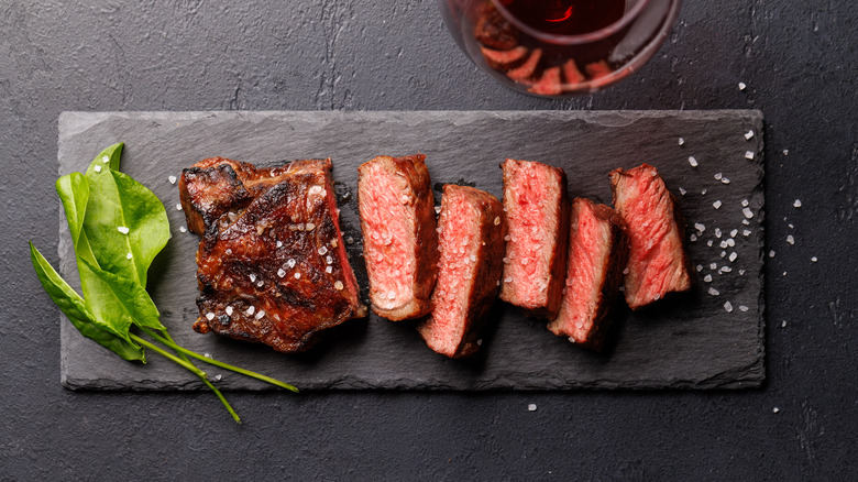 Sliced strip steak on a grey slate slab garnished with coarse salt