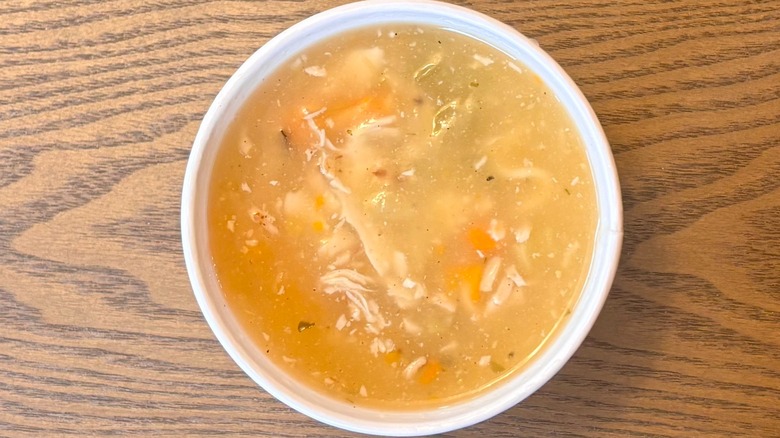 A cup of Chick-fil-A Chicken Noodle Soup with carrots and chicken pieces