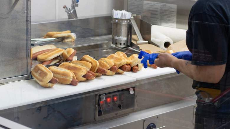 Costco employee puts on latex gloves in preparation for bagging hot dogs, 14 of which sit on the countertop