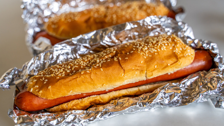Close-up of two Coscto hot dogs in sesame seed buns sitting on tin foil wrappers