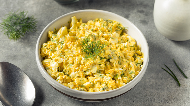Bowl of egg salad with dill and a spoon