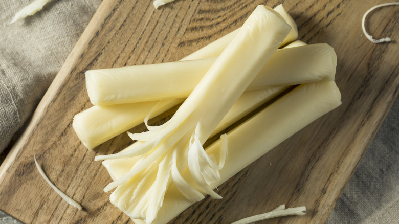 A small stack of string cheese, with one partially shredded, on a wooden plank