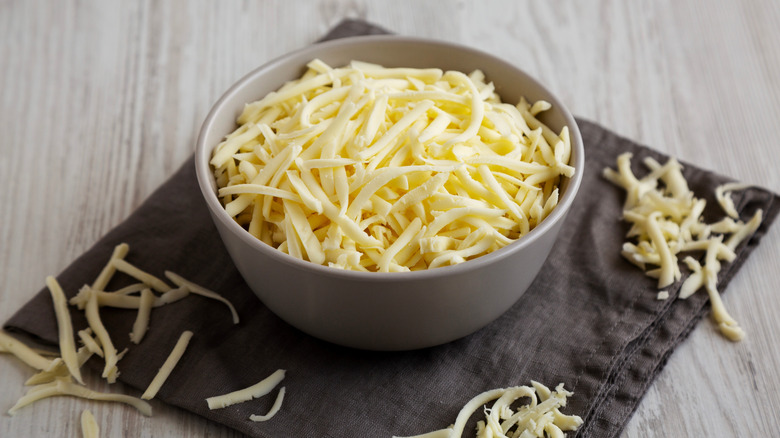 A gray bowl filled with pre-shredded mozzarella on top of a gray napkin