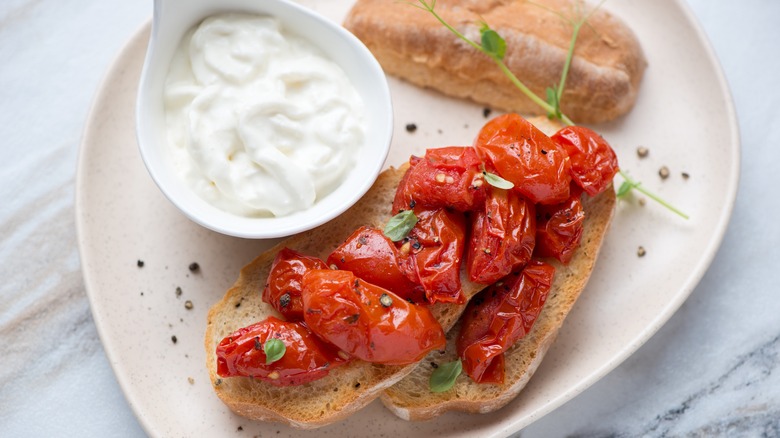 A white bowl with stracciatella next to crostini topped with roasted tomatoes