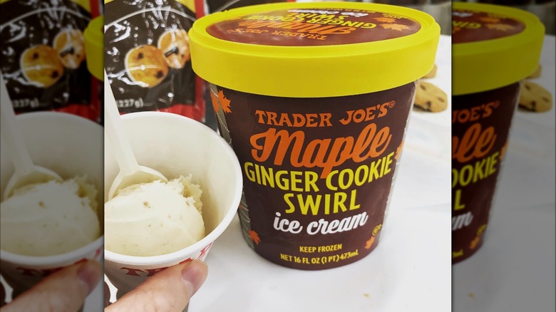 A hand holding a sample cup of Trader Joe's Maple Ginger Cookie Swirl Ice Cream next to the carton