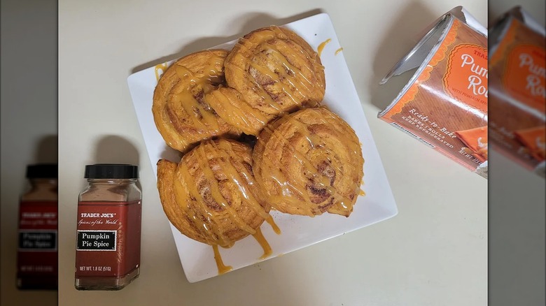 Four Pumpkin Rolls on a plate, drizzled with orange icing; the package and a jar of pumpkin pie spice off to the side