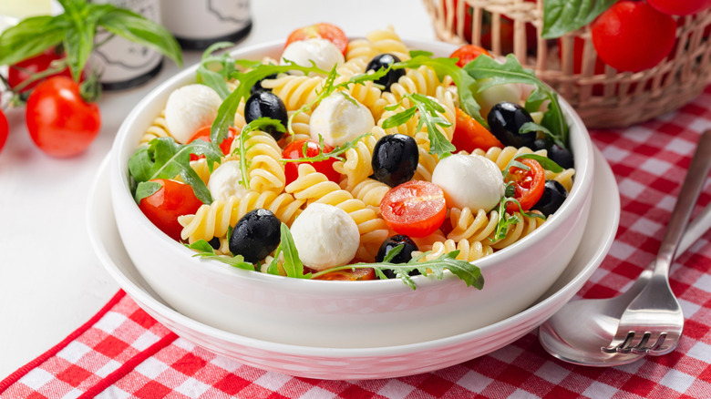 Cold pasta salad with fusilli, black olives, mozzarella, tomatoes, and arugula