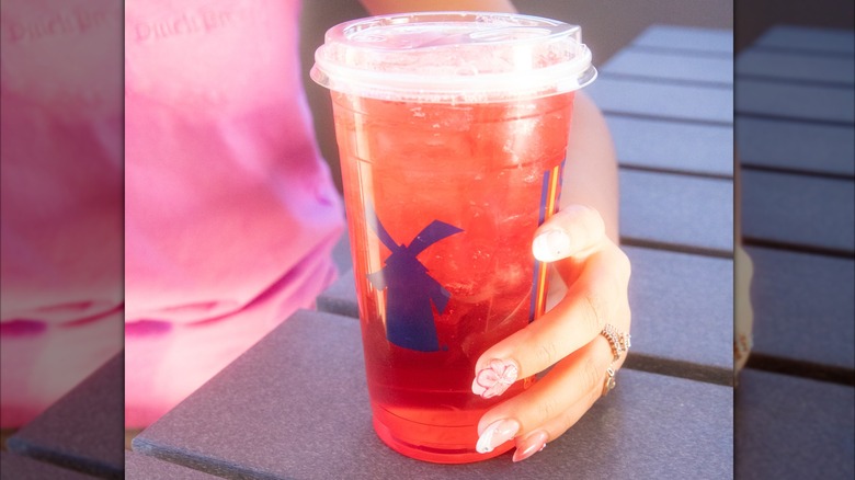 A woman holding a Dutch Bros Galaxy Fish drink at a picnic table