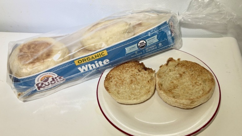 A package of Udi's White English Muffins leaning on a plate with a toasted muffin on it