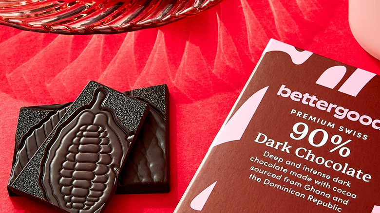 A Bettergoods 90% dark chocolate bar beside pieces of an opened bar on a red background