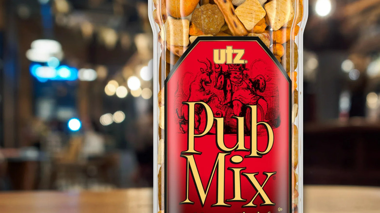 A close up picture of a container of Utz Pub Mix on a table with a blurred bar background