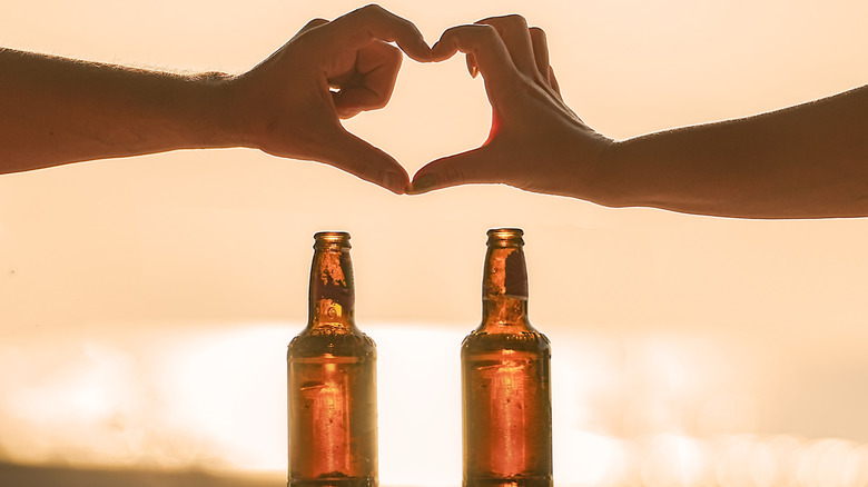 Two people forming a heart with their hands over a couple beer bottles on the beach