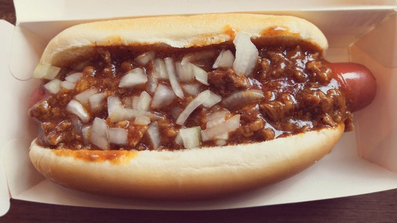 Hand holding A&W chili hot dog with glass of root beer blurred in background