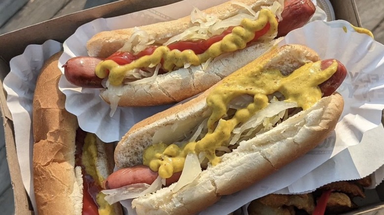 three hot dogs dressed with mustard in brown box