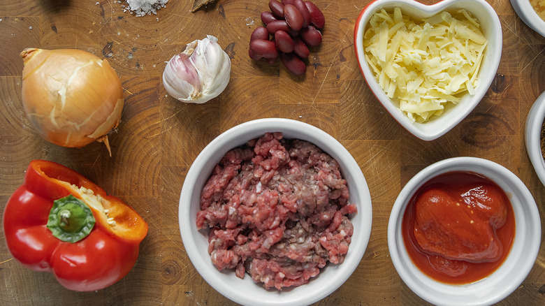 Various ingredients, such as ground beef, bell pepper, cheese, beans, and onion, on a cutting board