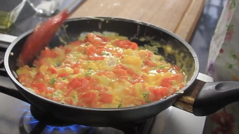Eggs being scrambled with tomatoes, onions, and peppers in a pan