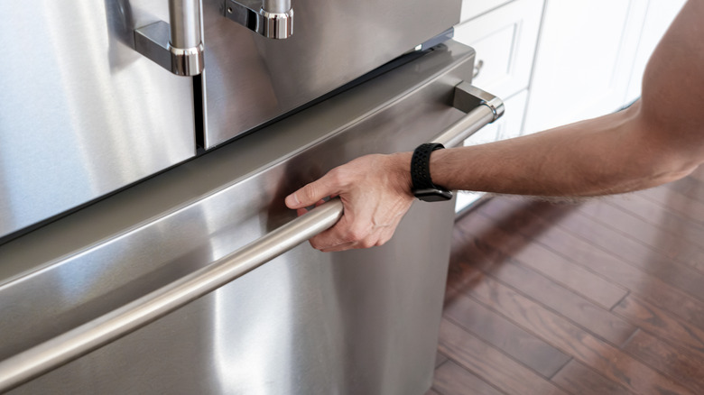 A person grips the handle of a stainless steel freezer