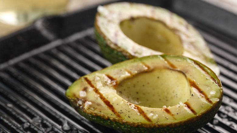 Two halves of an avocado on a grill