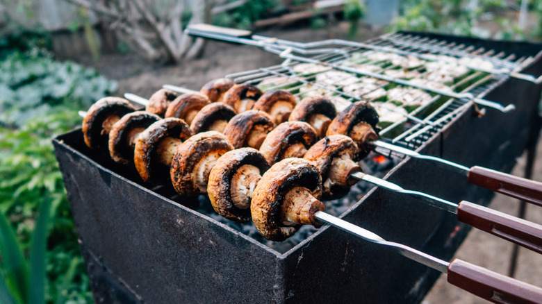Three metal skewers of mushrooms on a grill