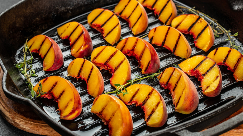 Slices of grilled peaches on a pan with herbs
