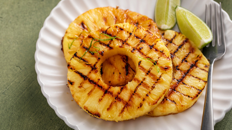 Two pieces of grilled pineapple on a white plate with sliced lime