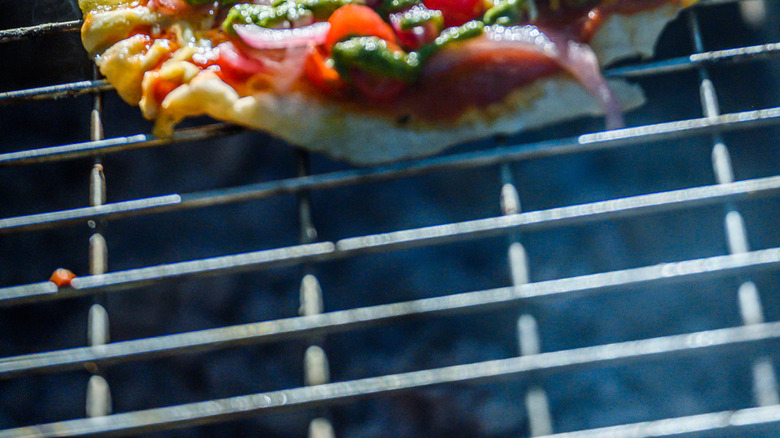 A close up of a pizza with veggies and pesto drizzle on grates