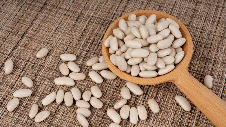 Cannellini beans spilling from a wooden spoon onto a woven mat