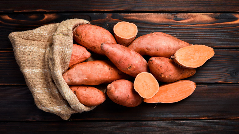 Bag of sweet potatoes spilling out onto wooden surface