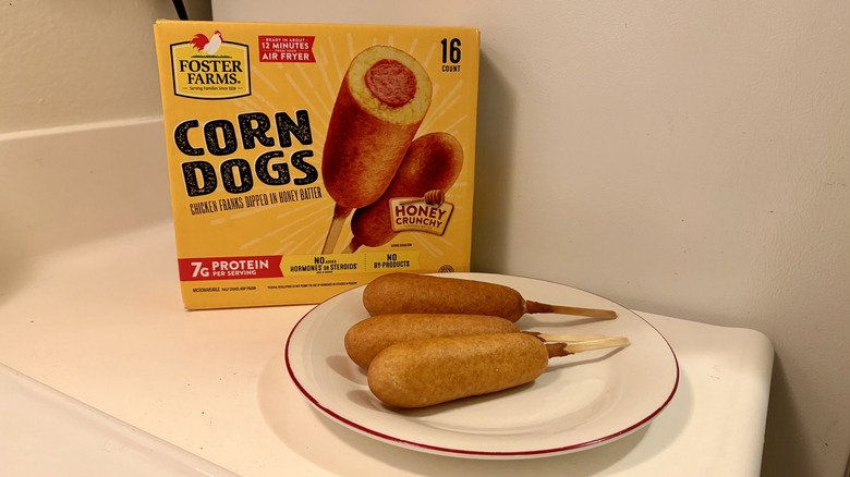 A plate of prepared Foster Farms Frozen Chicken Corn Dogs next to the box