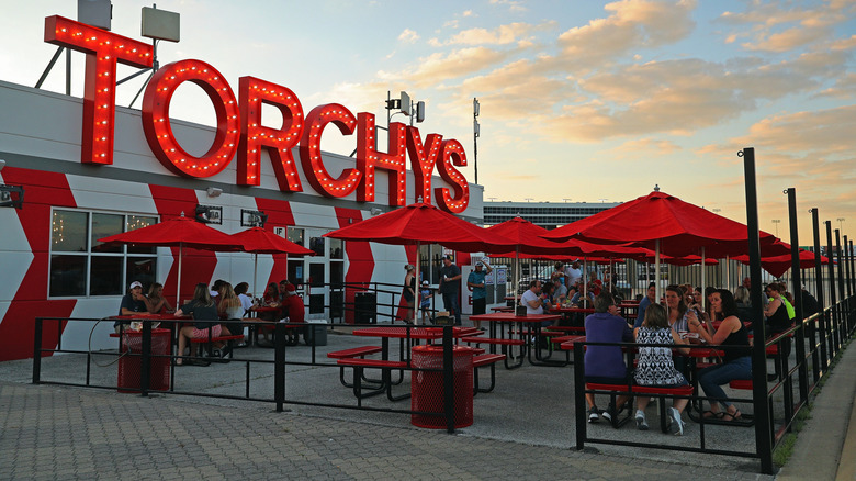 Outside dining area of a seaside Torchy's with a large red restaurant sign in the background