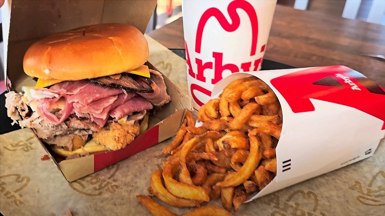 Arby's Meat Mountain sandwich stacked with meats, served with curly fries and a soft drink on a tray