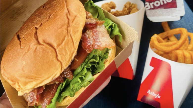 Arby's BLT-style sandwich with lettuce, tomato, and bacon, served with curly fries, fried chicken bites, a Bronco Berry sauce cup, and a mint shake.