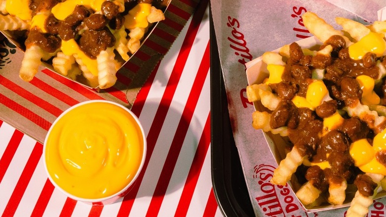 Portillo's Chili cheese fries with a side of cheese sauce on red and white striped table