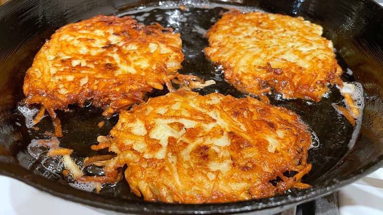 A pan of three potato latkes being fried