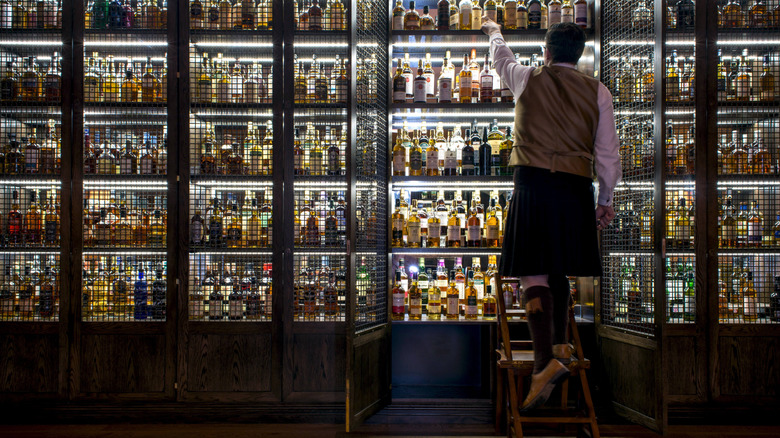 Man in kilt reaches for bottle of Scotch