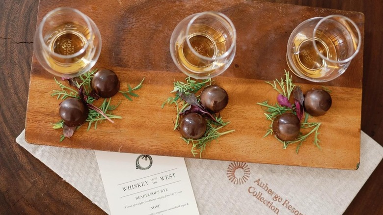 Three glasses of whiskey on a wooden cutting board with chocolate truffles