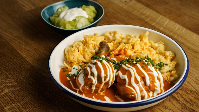 Chicken paprikash drizzled with sour cream alongside a side of dumplings and cucumber salad.