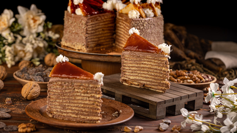 Dobos torte presented whole and sliced, with component ingredients artfully arranged behind.