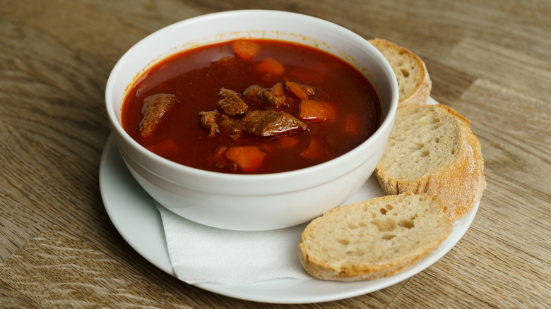 Hungarian goulash with sliced bread on a wooden dining table.