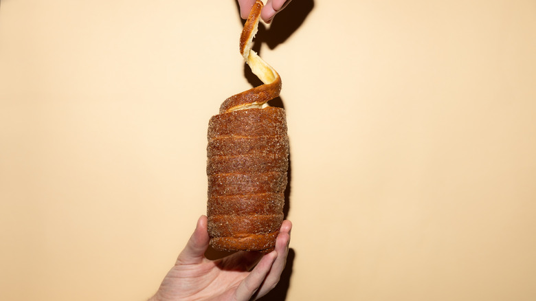A hand holding and pulling apart a kürtőskalács on a beige background.