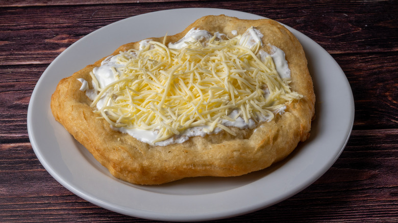 A plate of lángos topped with cheese and sour cream.