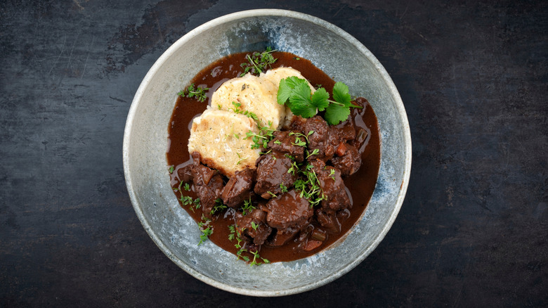 Pörkölt with bread dumplings garnished with fresh herbs.