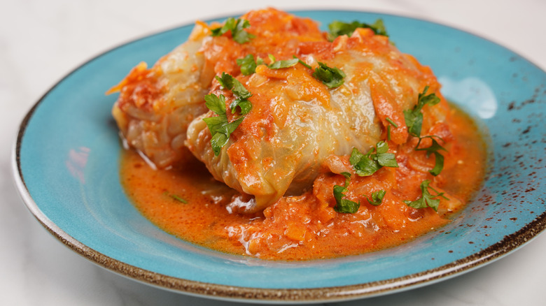 A plate of cabbage rolls covered in a tomato sauce and topped with fresh herbs.